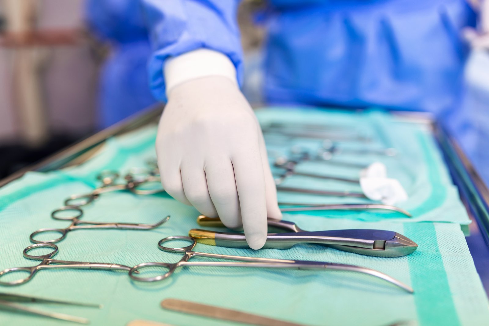 Surgeon picking up surgical tool from tray. Surgeon is preparing for surgery in operating room. He is in a hospital. عيادة الجراحة العامة